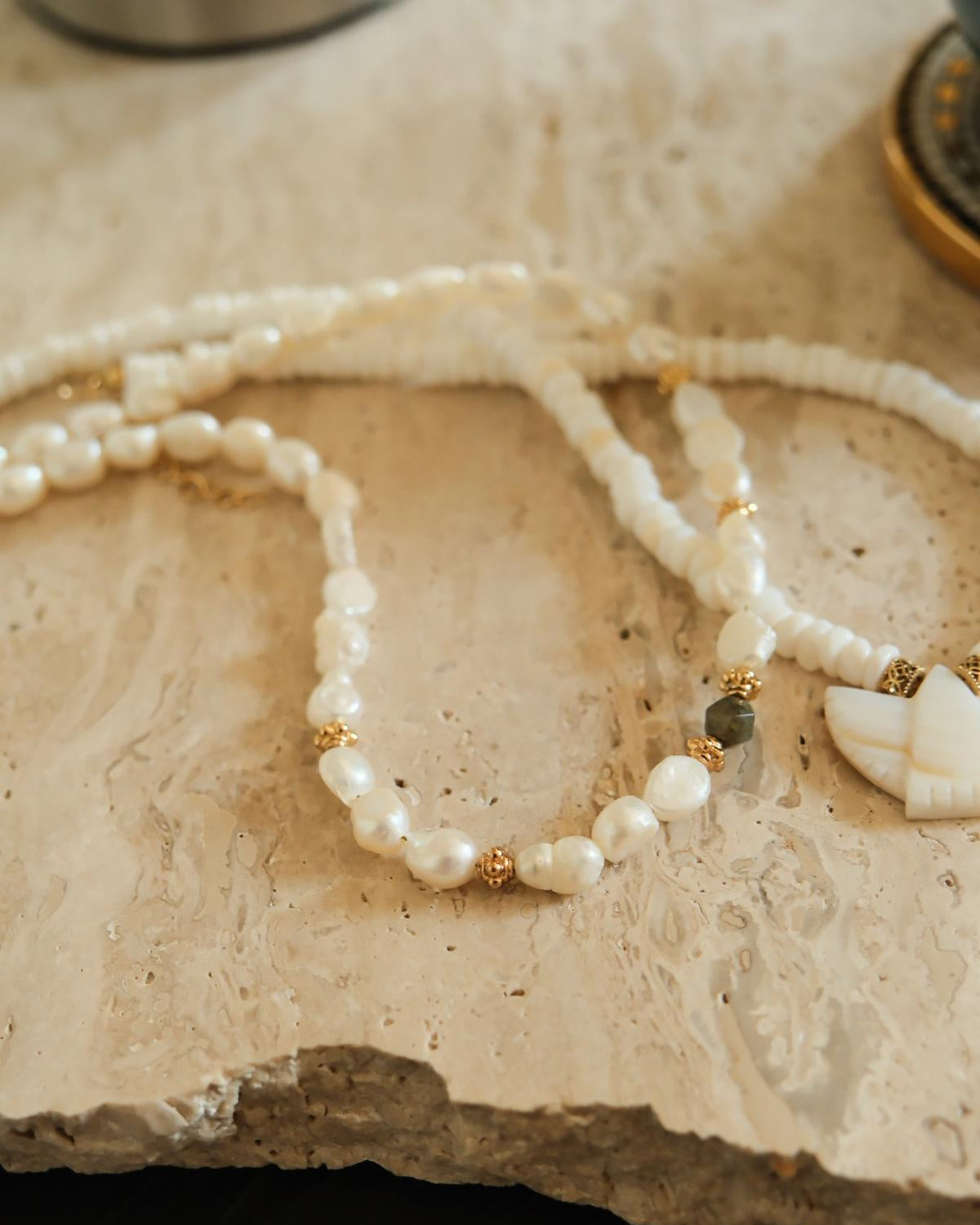 Collier en perles d'eau douce et perle en labradorite posé sur plan de travail granit beige détaillé