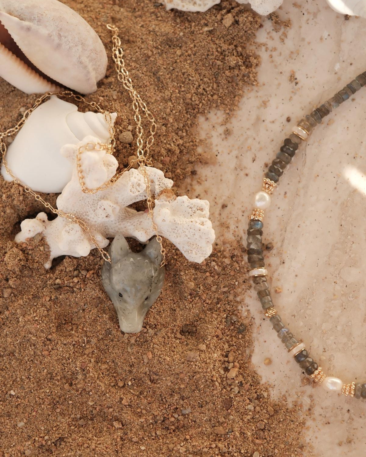 Détail collier en tête de loup sur chaine avec collier en perles heishi labradorite sur sable et corail
