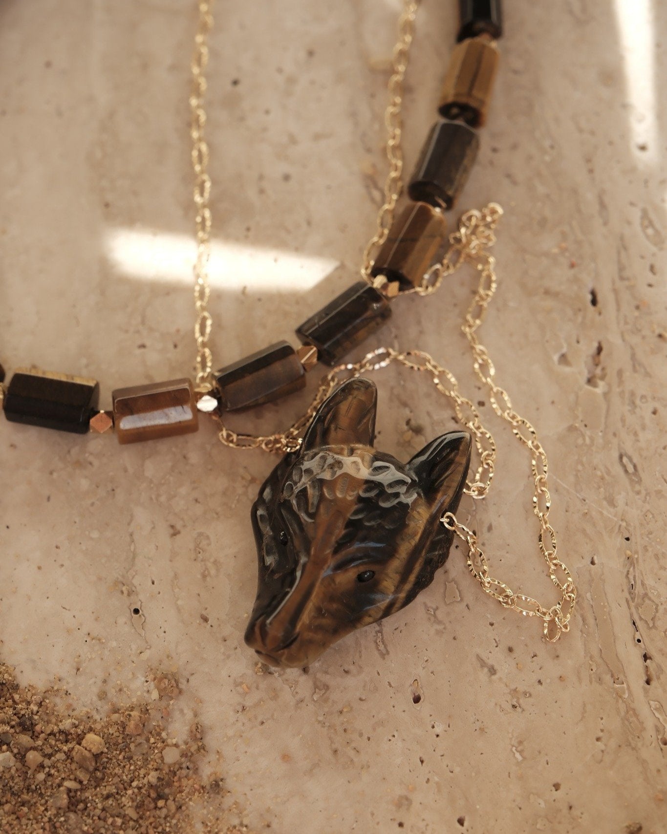 Collier loup en œil de tigre doré sur fond en pierre beige, bijou semi-précieux Atelier Veda.