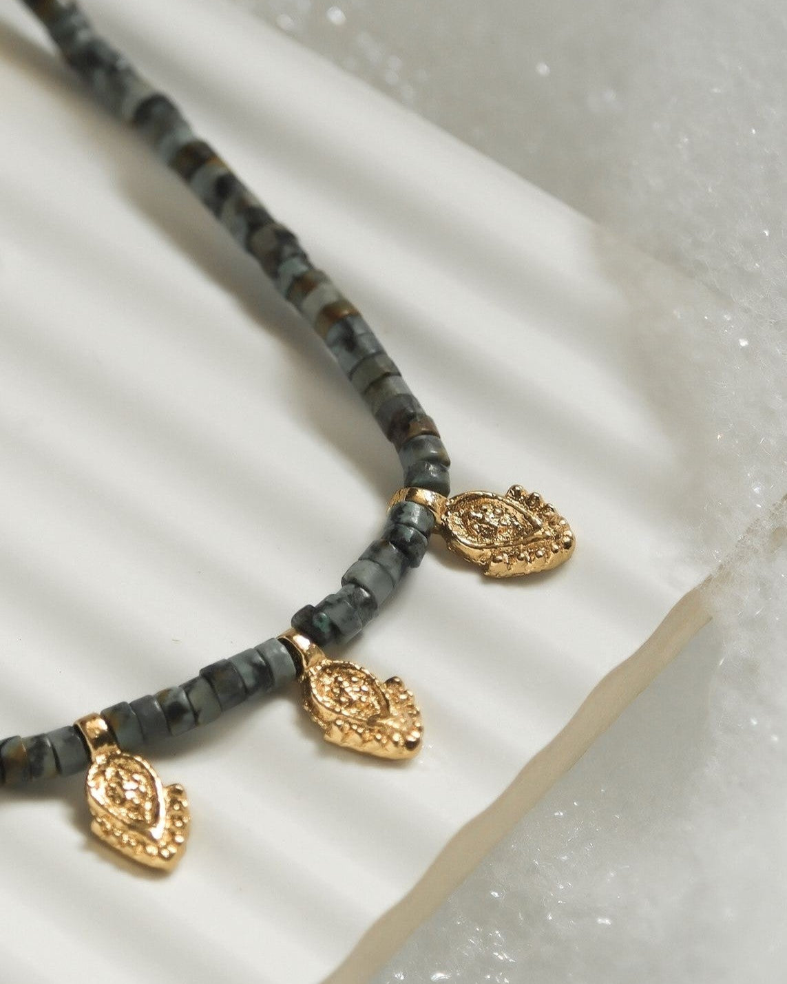 Collier en perles de turquoise africaine posé sur plan blanc avec détails des trois pendentifs indiens dorés à l'or fin 
